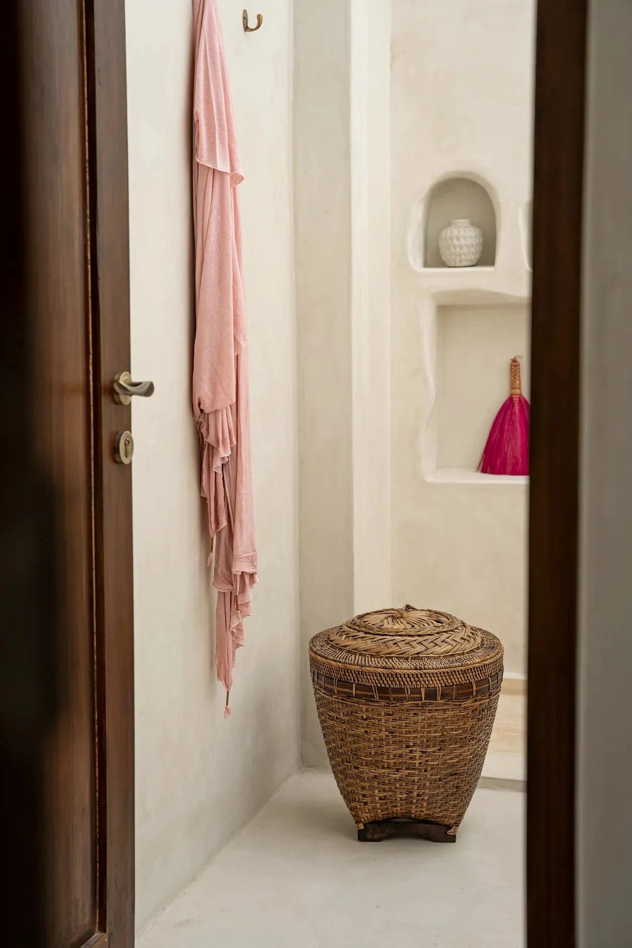 Bathroom interior with a wicker stool, pink towel, and decorative vase.