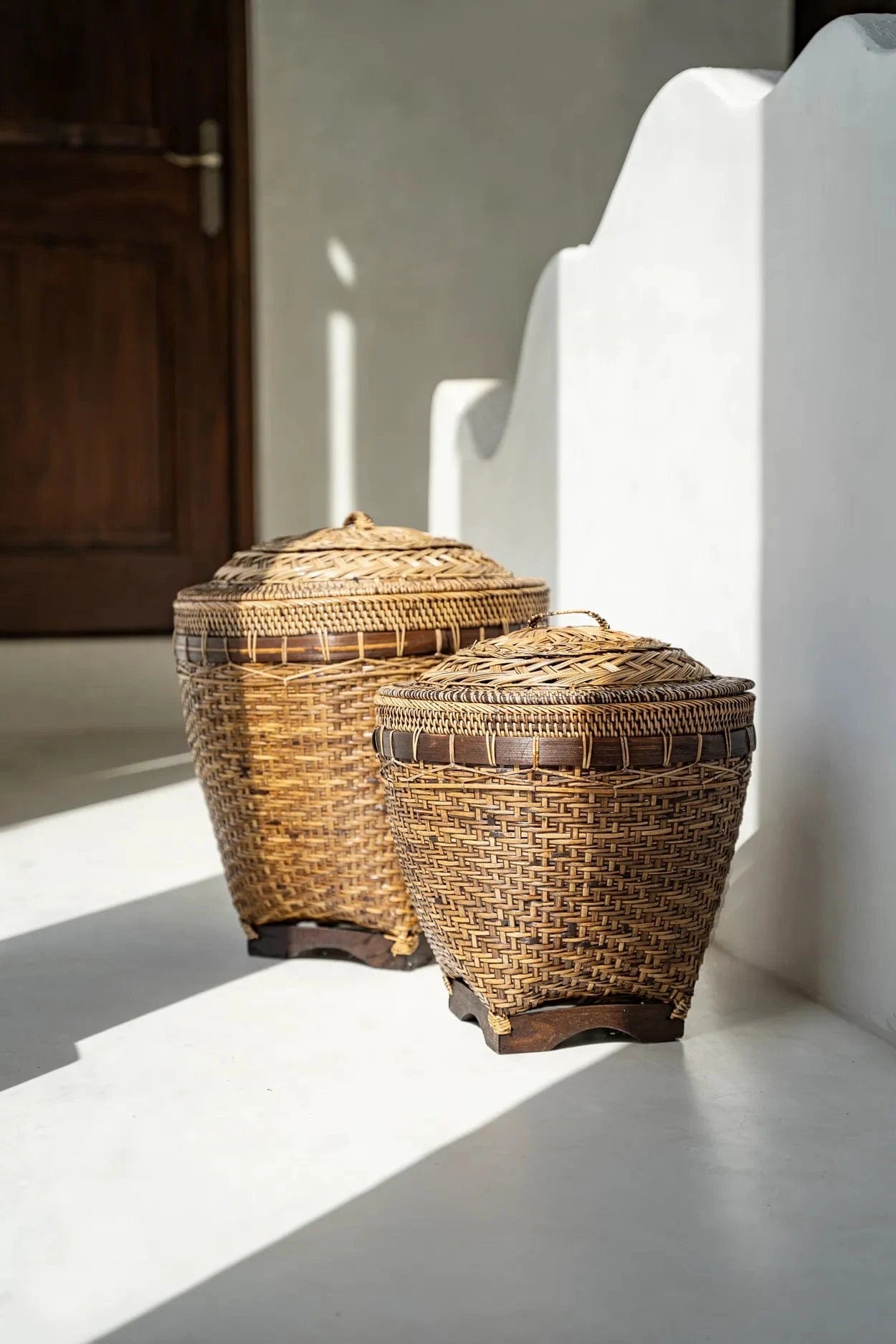 Two wicker baskets with lids on a white surface with a neutral background