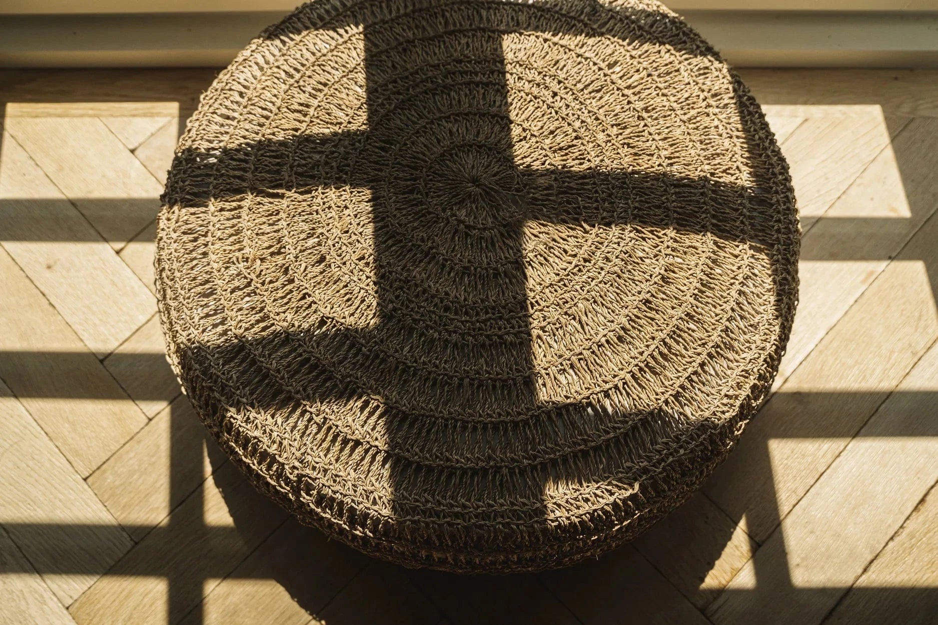 Round woven mat on a wooden floor with sunlight casting shadows