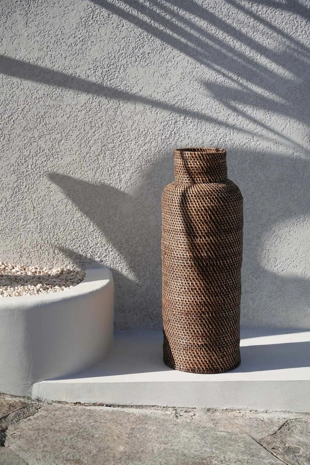 Woven umbrella stand on a ledge with a textured wall background