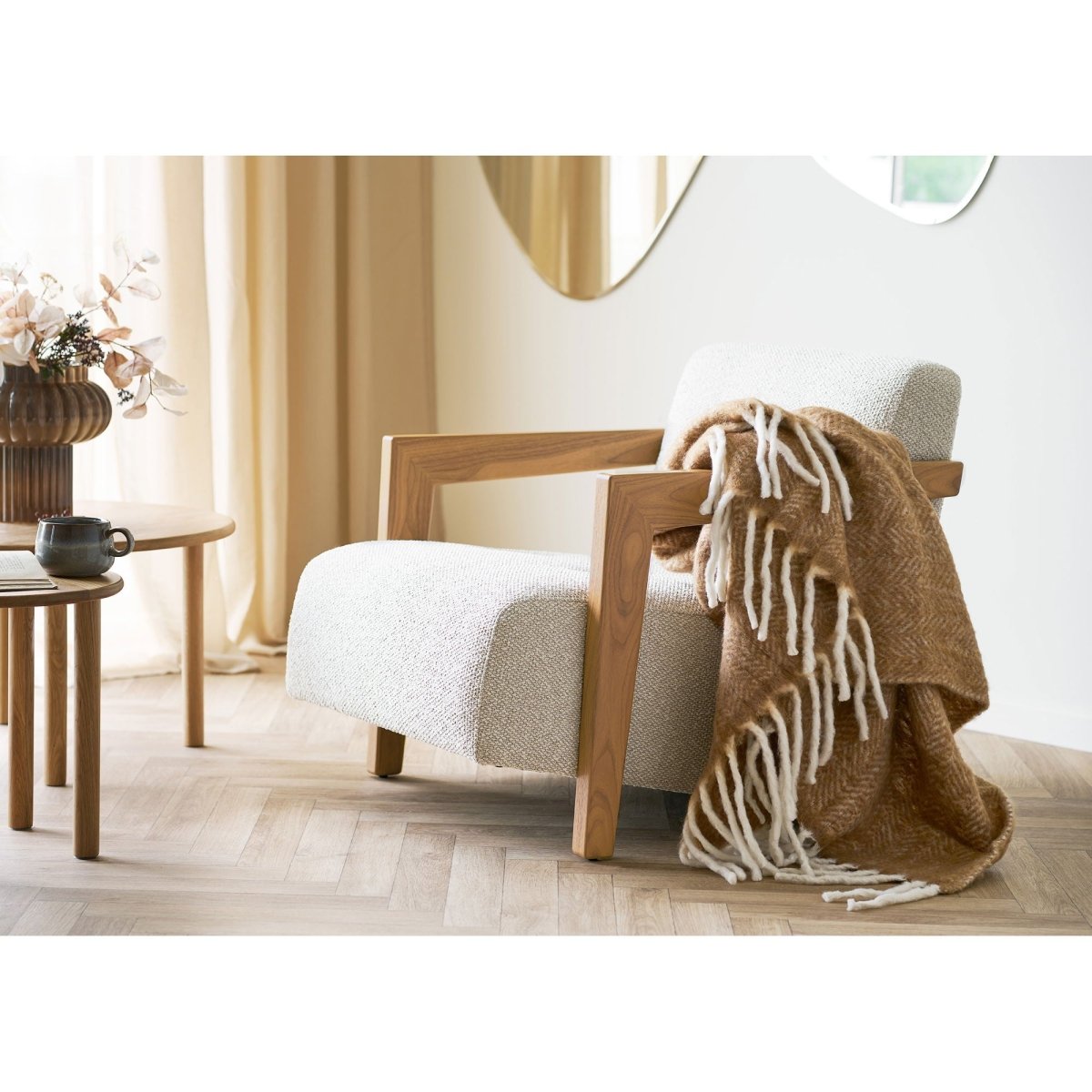 Wooden armchair with a white cushion and brown blanket in a room with light-colored walls and decor.