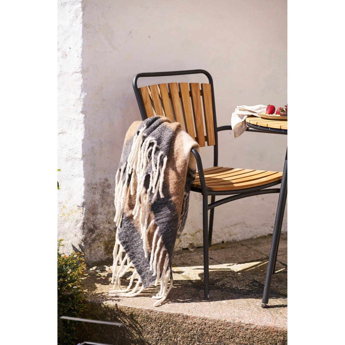 Wooden chair with a blanket draped over it against a white wall.