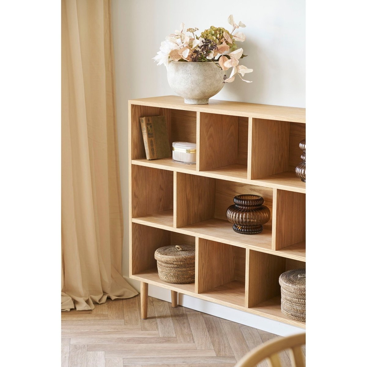 Wooden shelf with decorative items in a room with curtains and a chair.