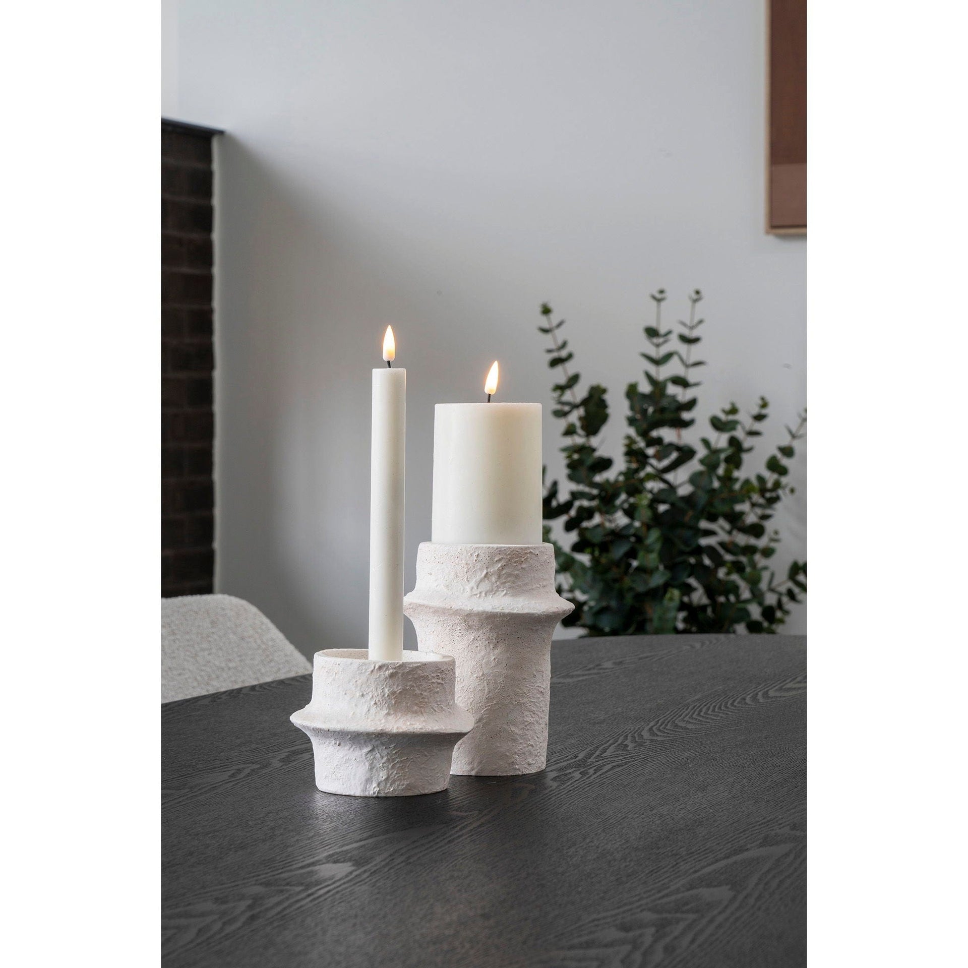 Two white candles in textured concrete holders on a dark surface.