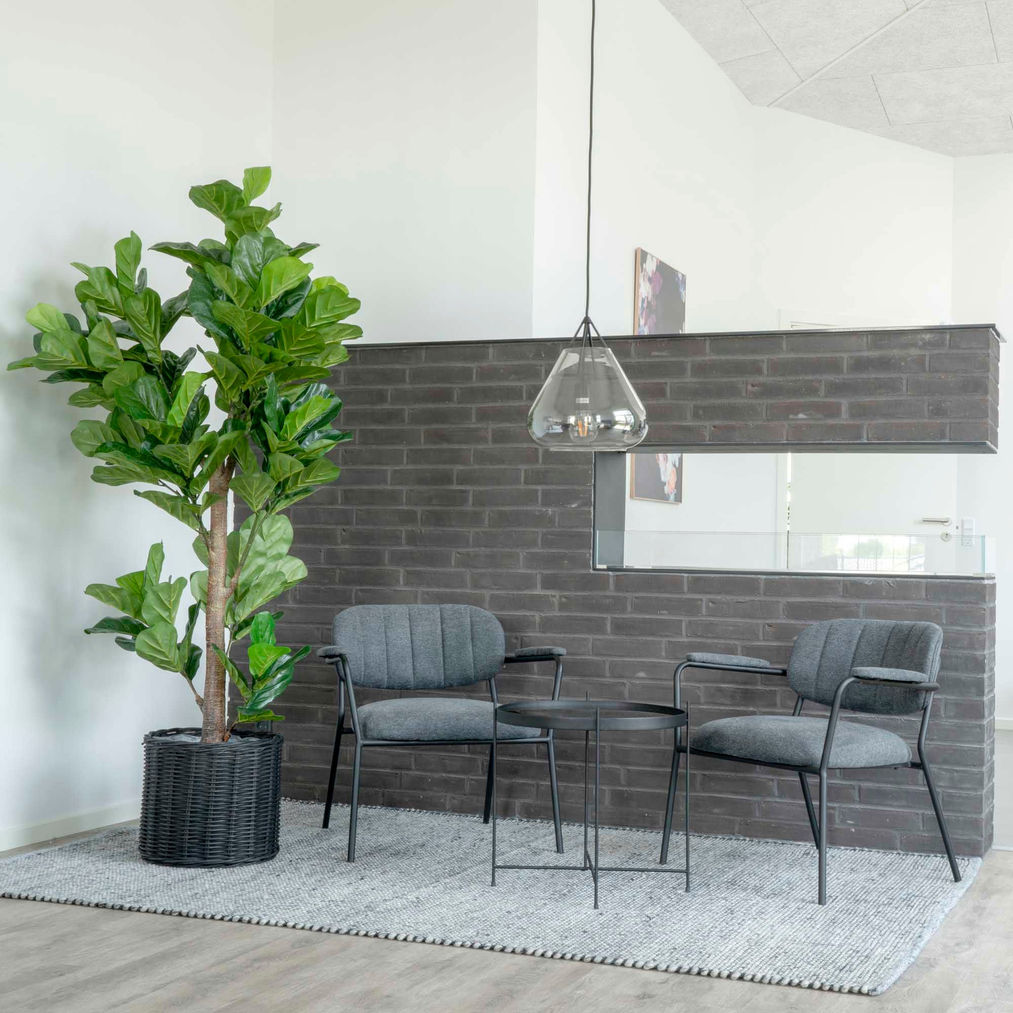 Modern outdoor seating area with gray chairs, a small table, and a potted plant against a brick wall.