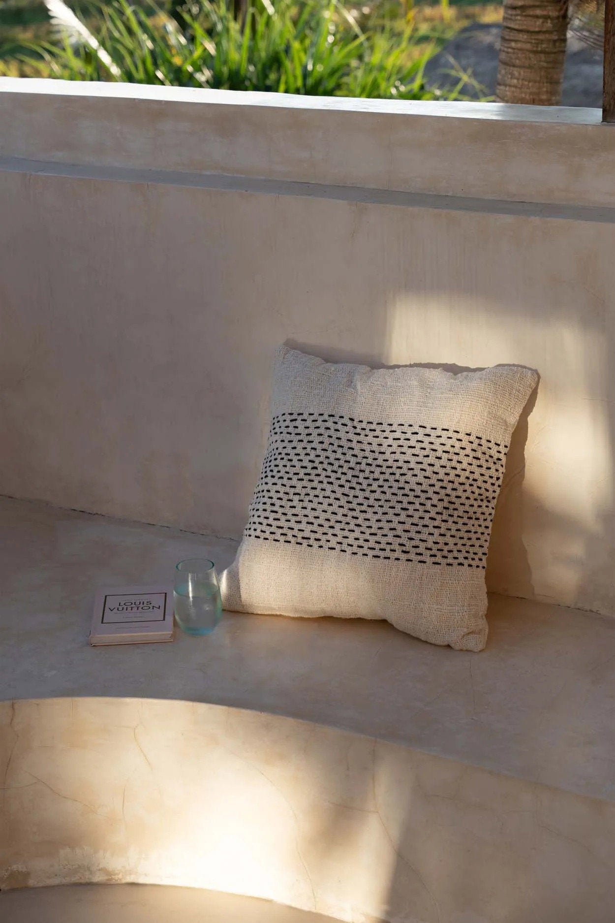 Beige cushion with a textured pattern on a beige surface, with a small bottle and box in the background.