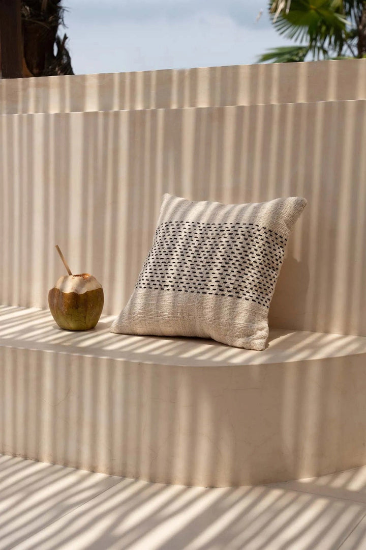 Decorative pillow with a geometric pattern on a textured wall with a coconut and palm leaves in the background.
