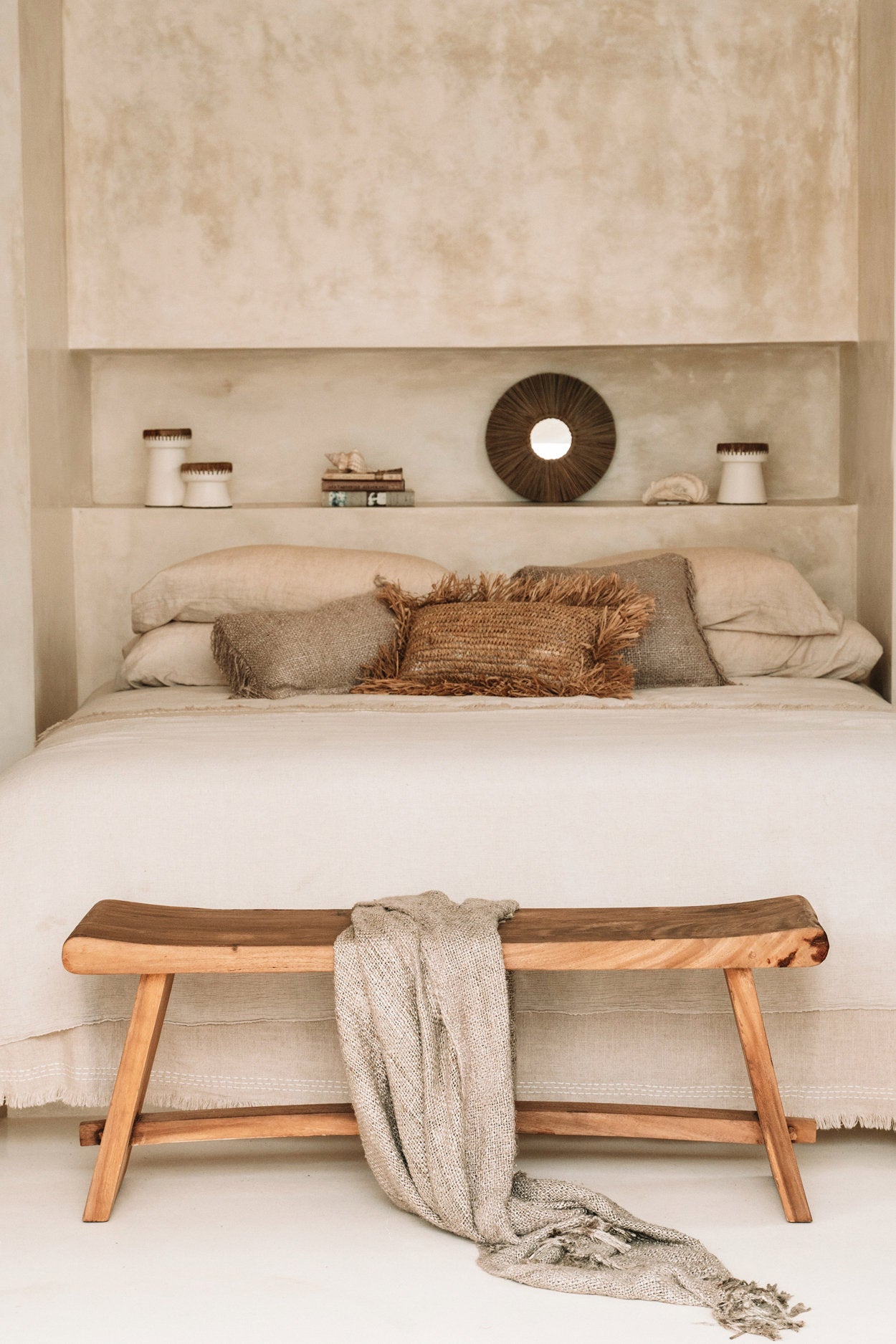 Beige bedroom with a bed, wooden bench, and decorative items.