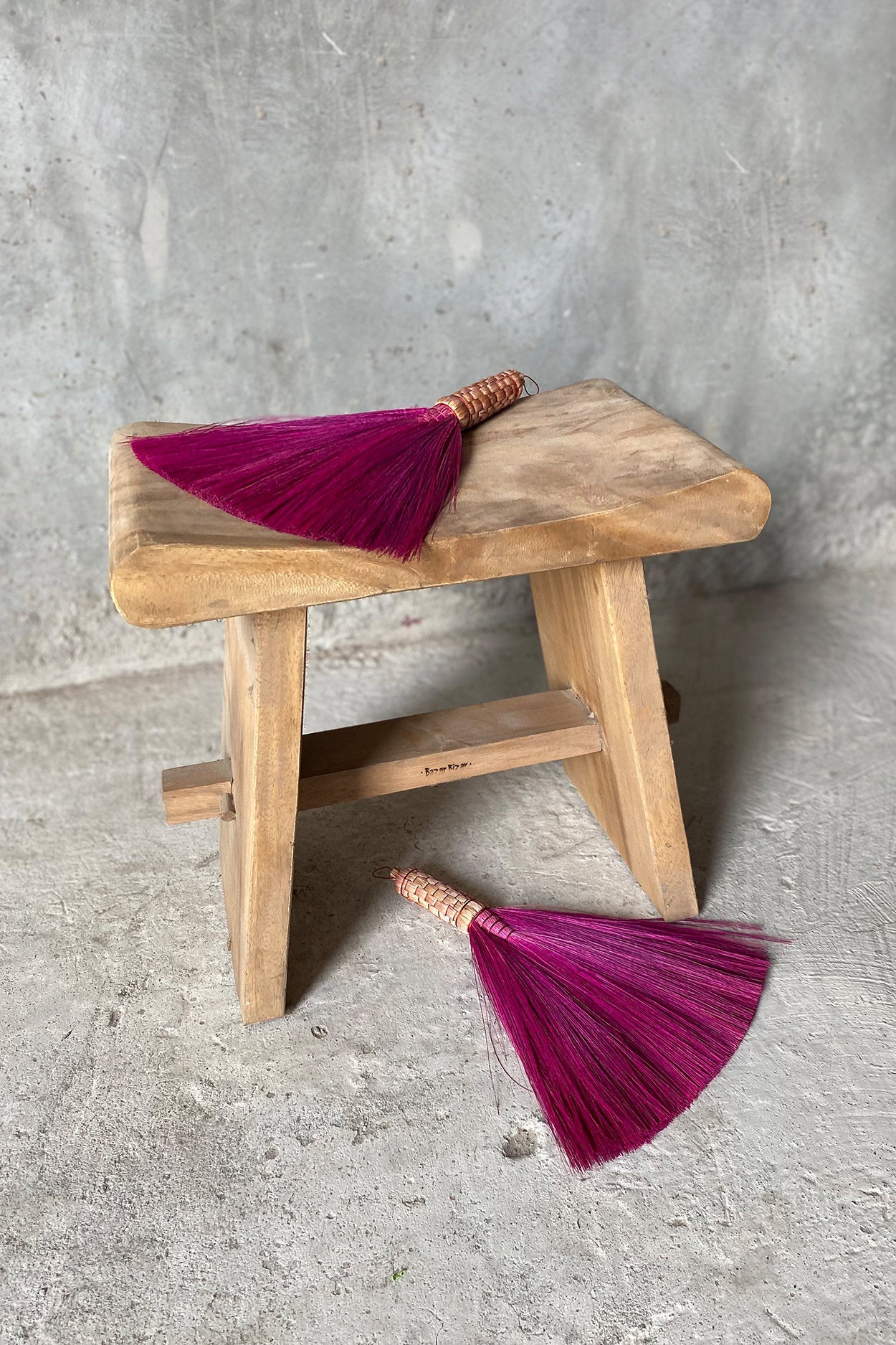 Wooden stool with a pink tassel on a concrete floor