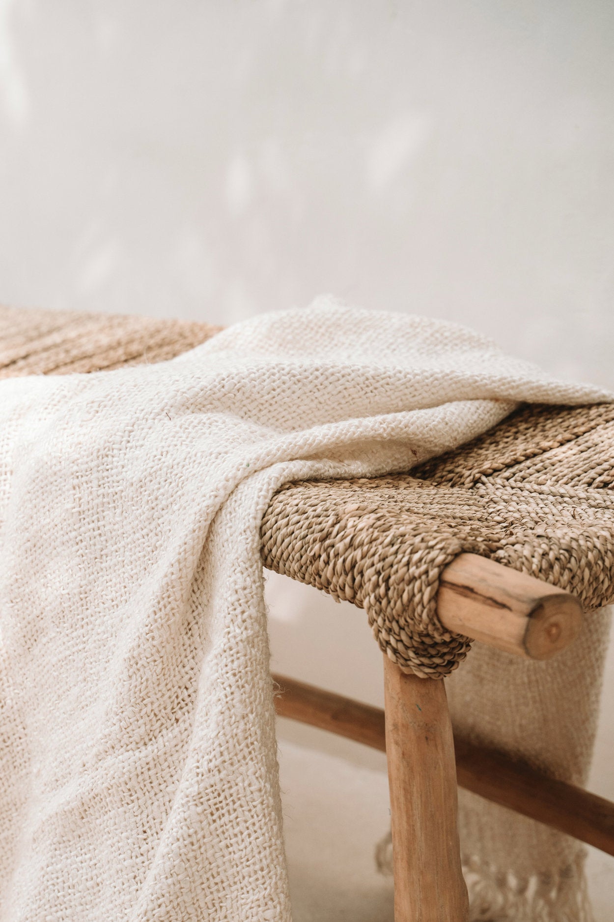 Beige textured blanket draped over a woven chair with a neutral background
