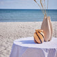 "Stylish Olivia round tablecloth on a beachfront table overlooking the sea, perfect for seaside gatherings."