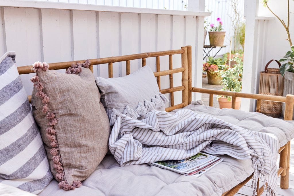 Oville Cushion 50x50 cm Dark Linen with tassels on rustic bench.