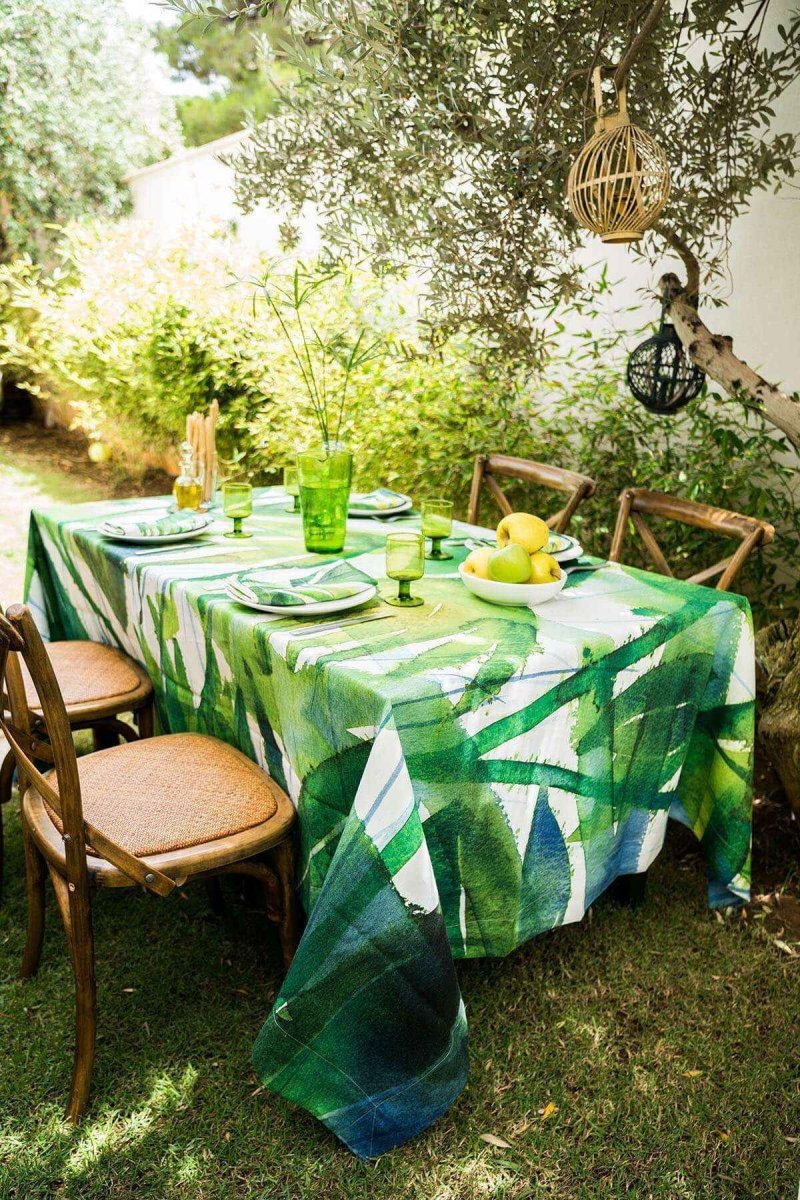 Outdoor dining table set with a green and white patterned tablecloth in a garden setting.