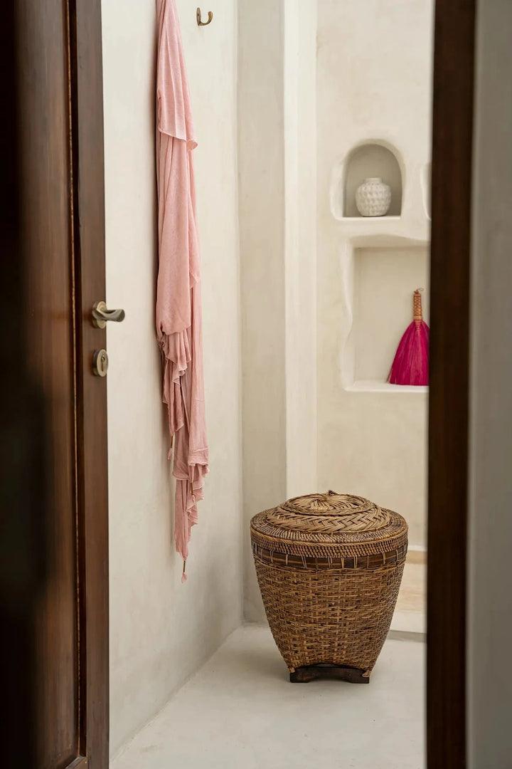 Bathroom interior with a wicker stool, pink towel, and decorative vase.