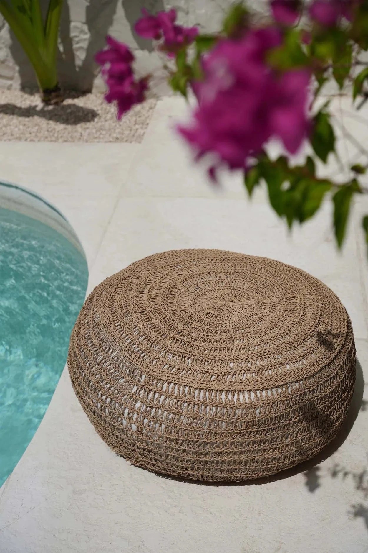 Woven brown ottoman by a pool with pink flowers in the background