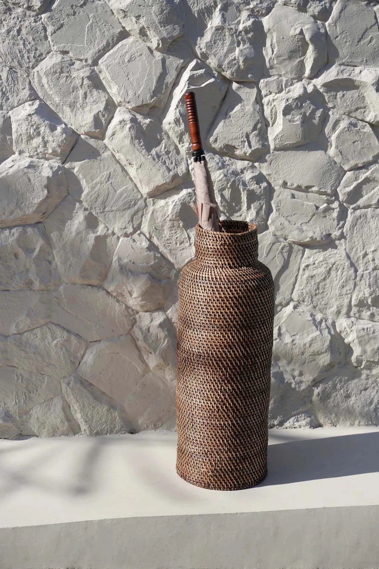 Woven umbrella stand against a stone wall