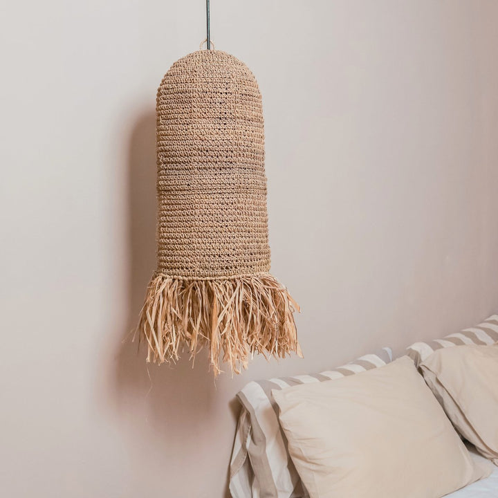 Woven pendant light with fringe hanging above a bed with striped bedding.