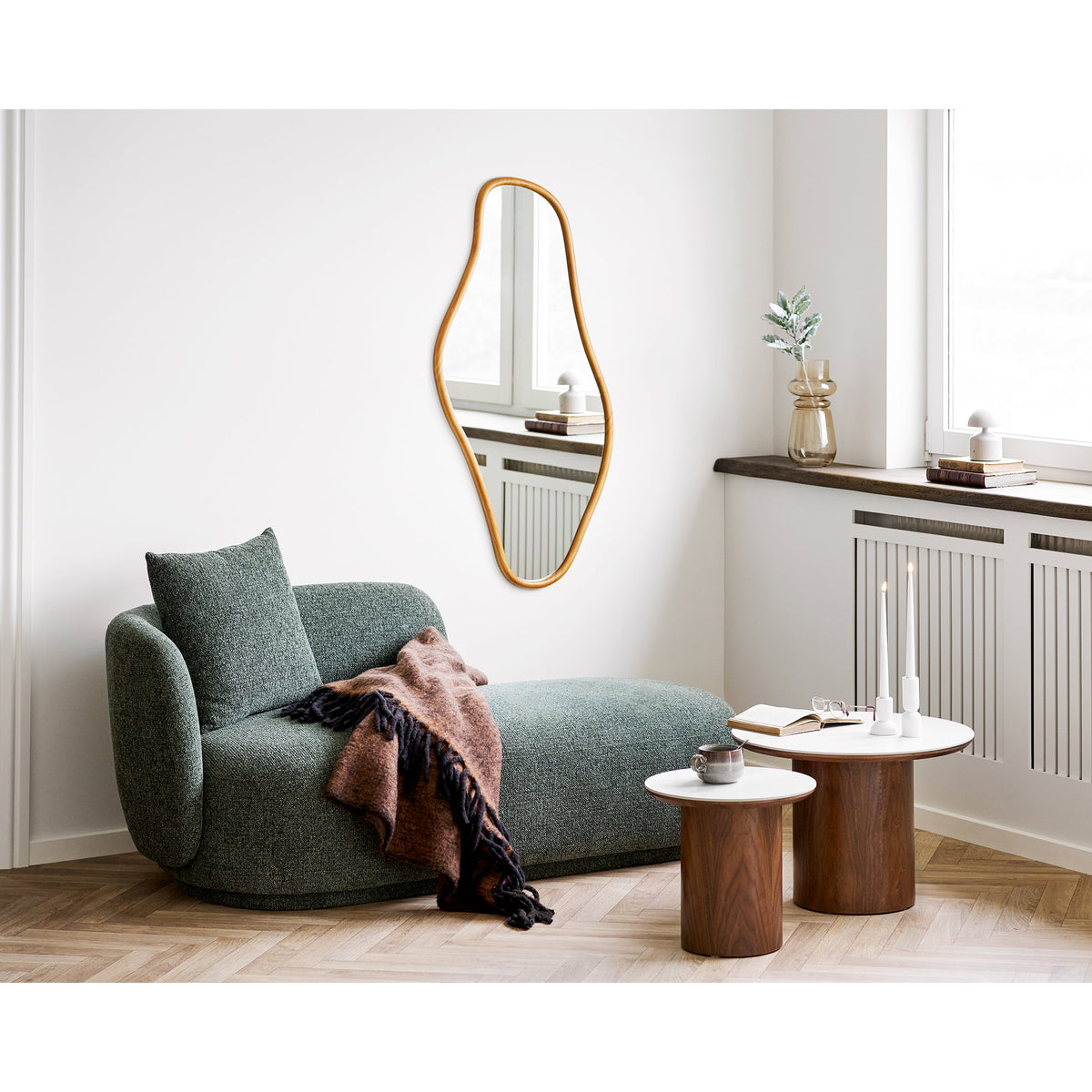Modern living room with a green sofa, wooden tables, and decorative mirror.