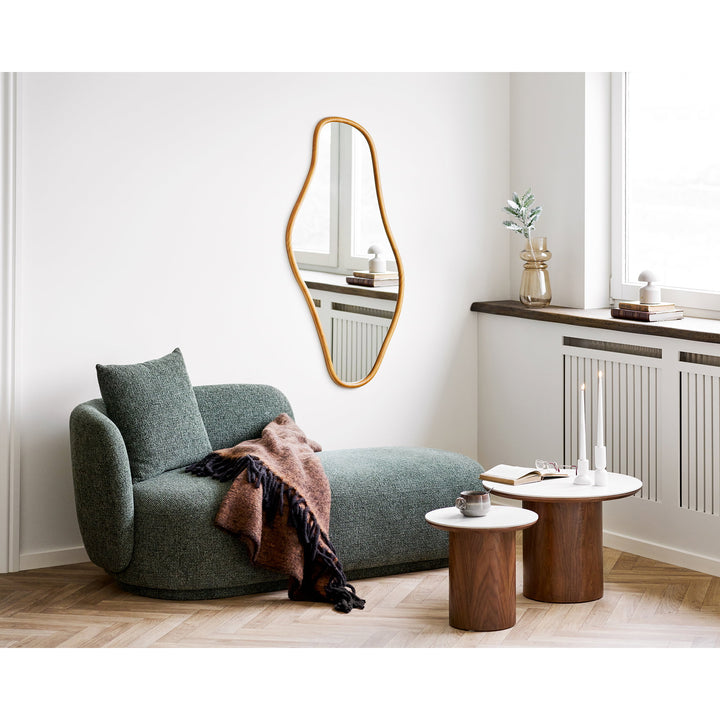 Modern living room with a green sofa, wooden tables, and decorative mirror.