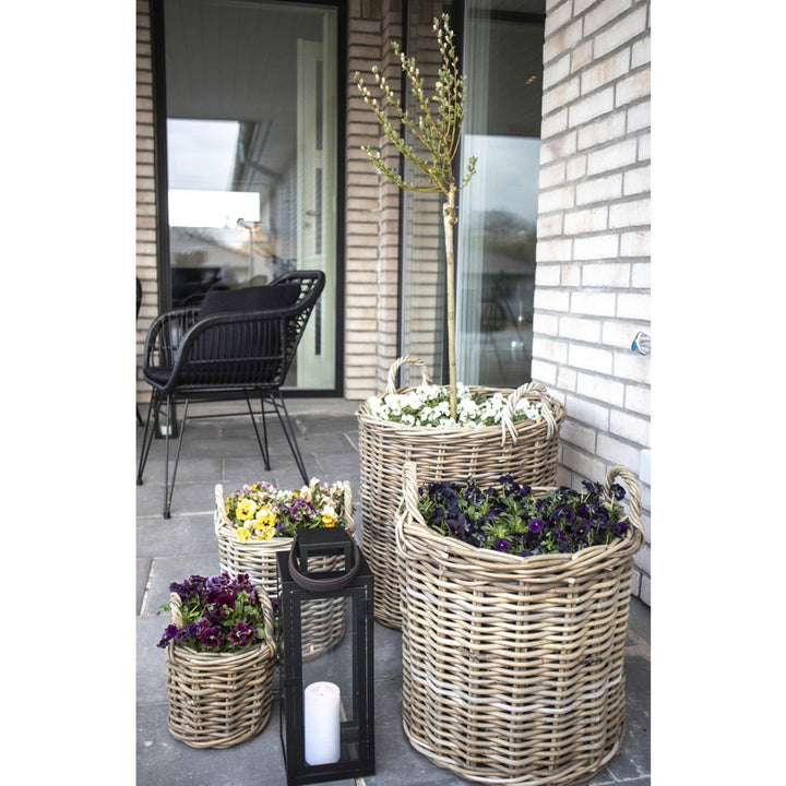 Wicker planters with flowers and a candle lantern on a patio.
