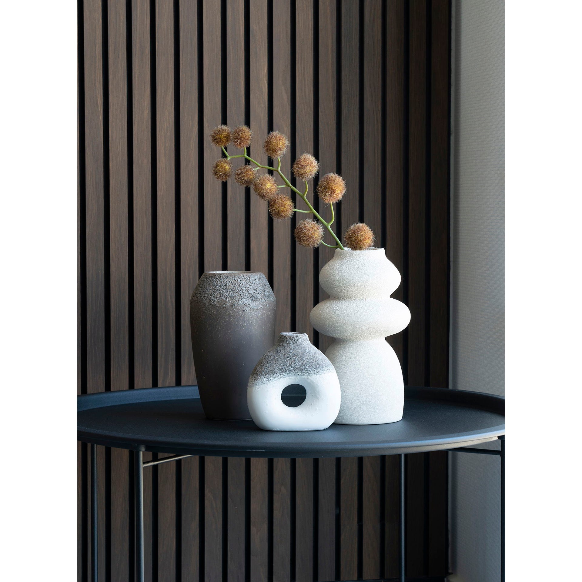 Three vases on a dark surface with a striped wall background