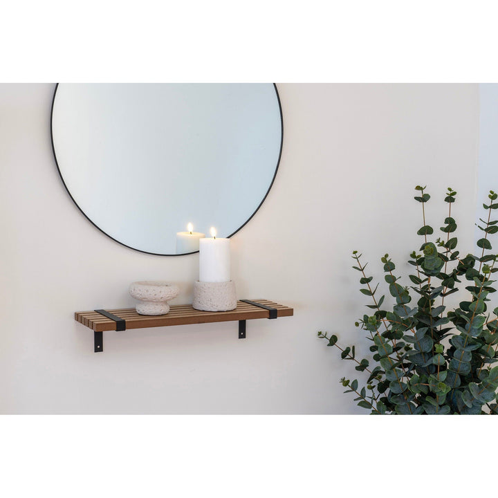Round mirror above a wooden shelf with a candle and decorative objects, next to a potted plant.
