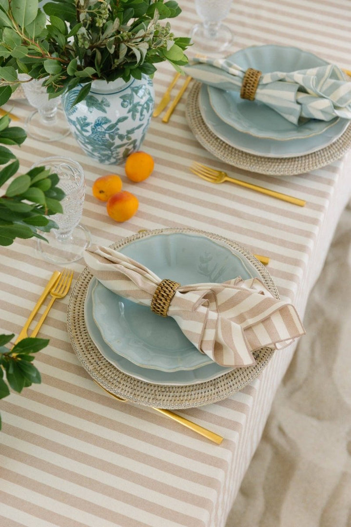A beige tablecloth with horizontal stripes laid out on a table accompanied by plates, cutlery, and a floral centerpiece.