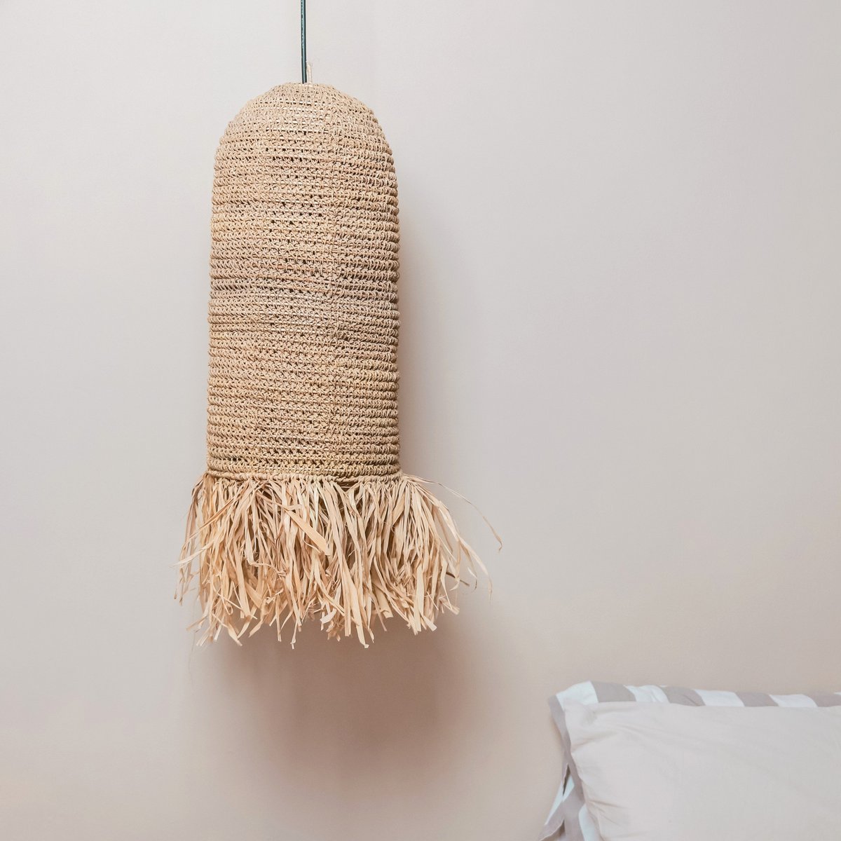 Woven pendant light with fringes on a plain wall