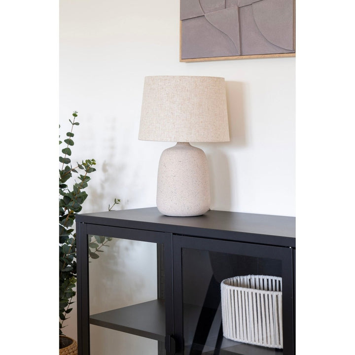 Table lamp on a black cabinet with a plant and basket in a room setting