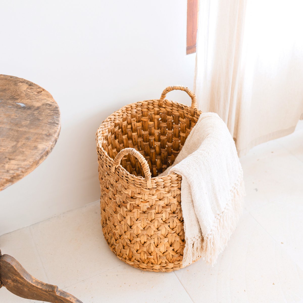 Woven basket with a white blanket on a light wooden floor.