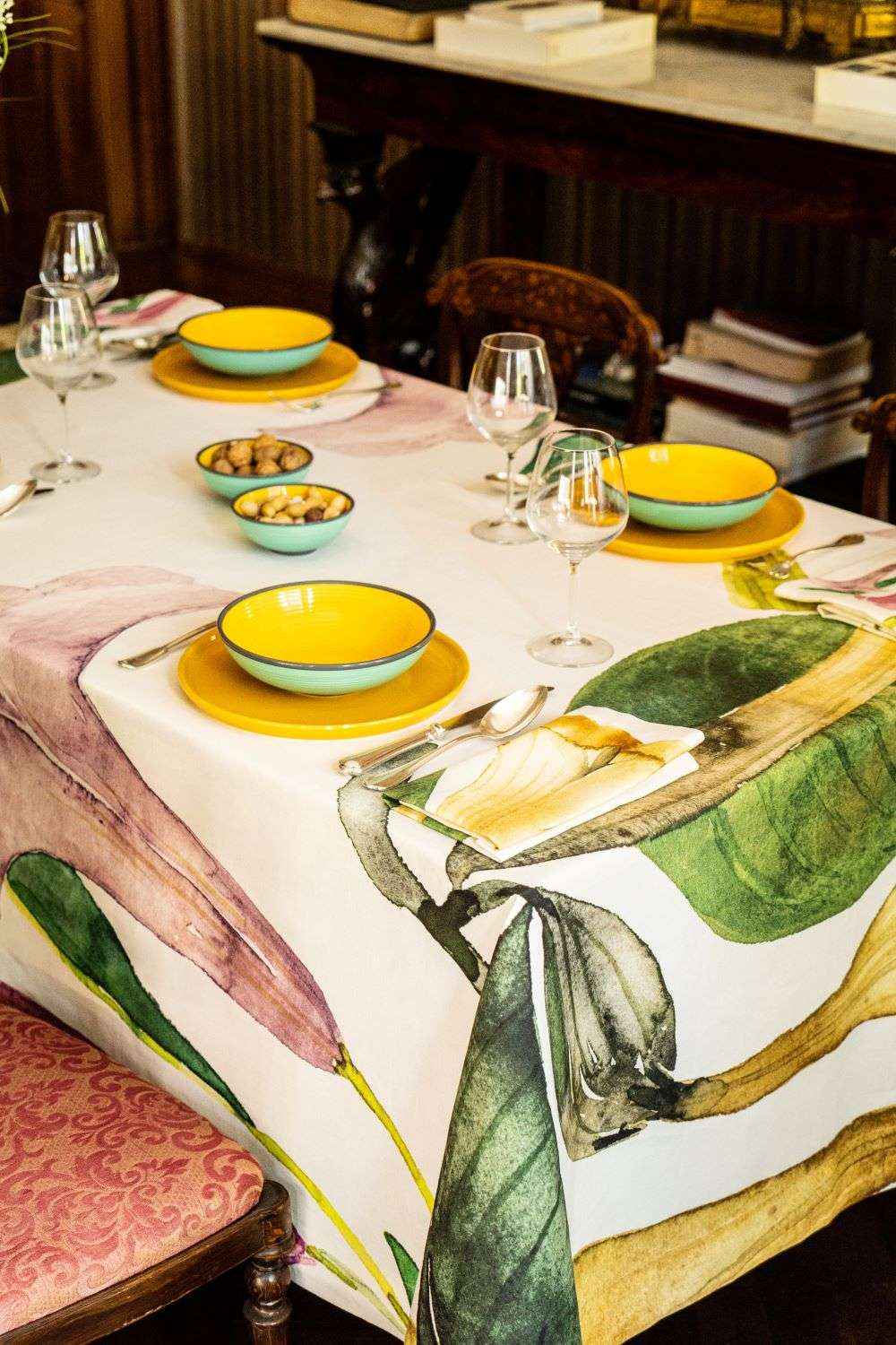 Dining table set with yellow plates, green leaves on a tablecloth, and wine glasses.