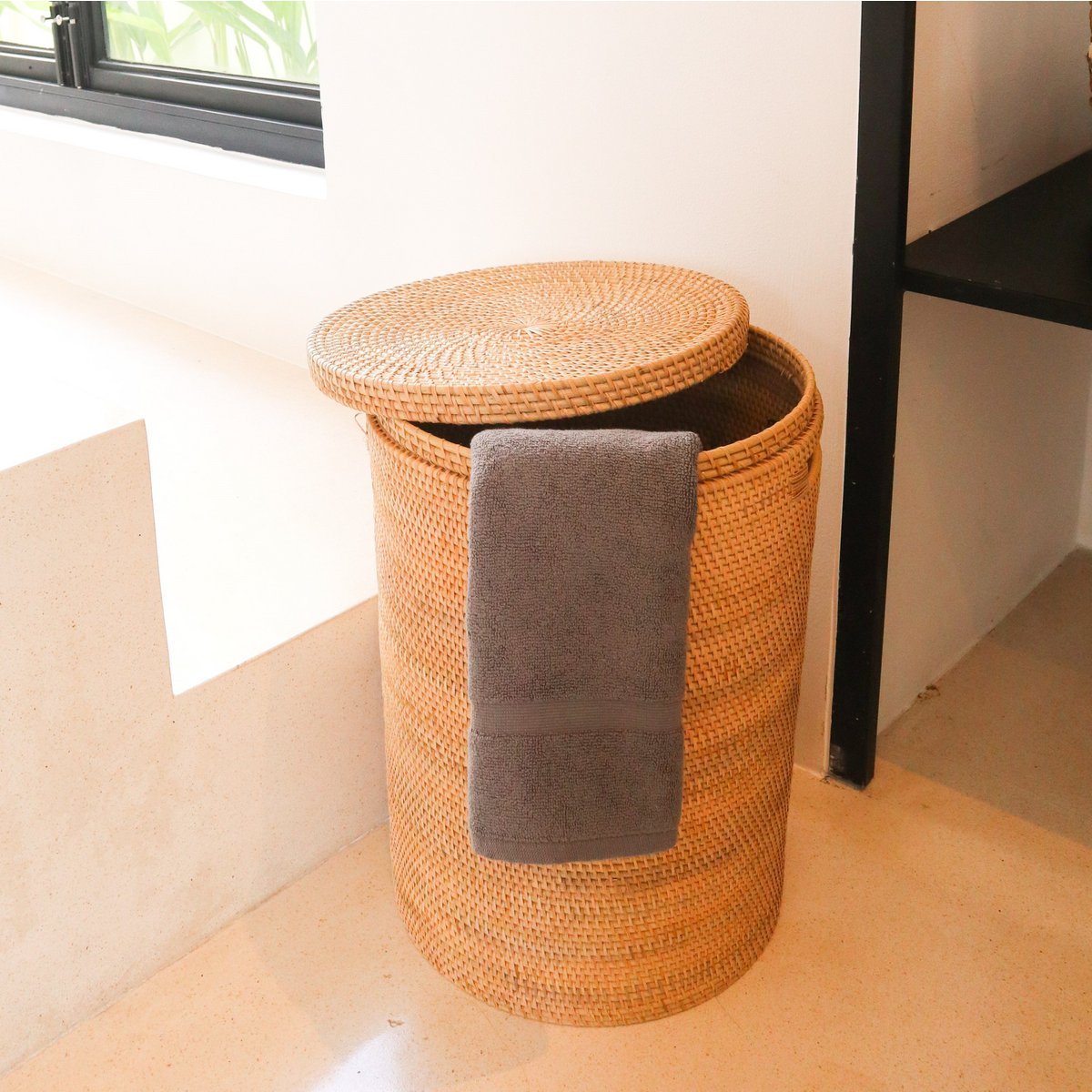 Woven laundry basket with a gray towel inside, placed on a light wooden floor.