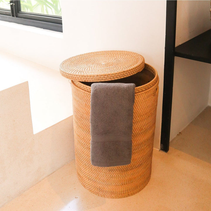 Woven laundry basket with a gray towel inside, placed on a light wooden floor.