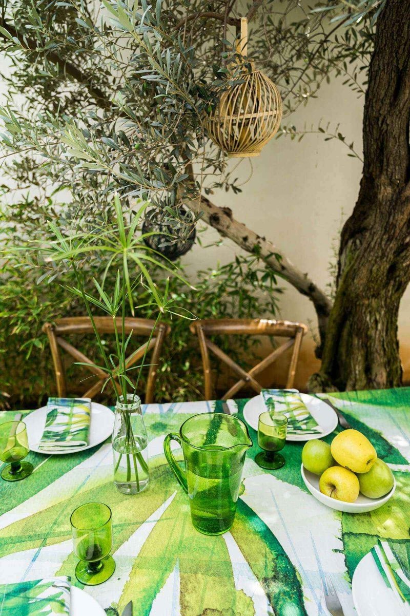 Outdoor setting with a table set for a meal, green tablecloth, and natural elements.