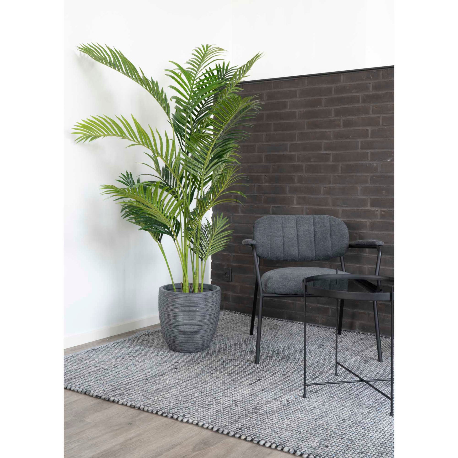 Potted plant in a room with a gray sofa and black brick wall.