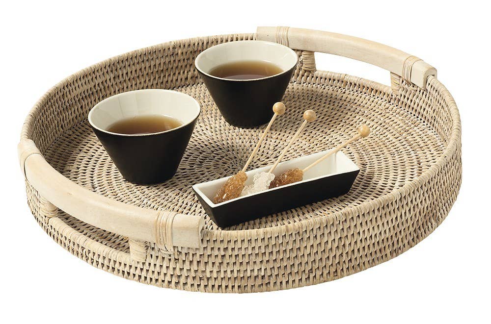 Woven tray with two black tea cups and a small dish on a white background