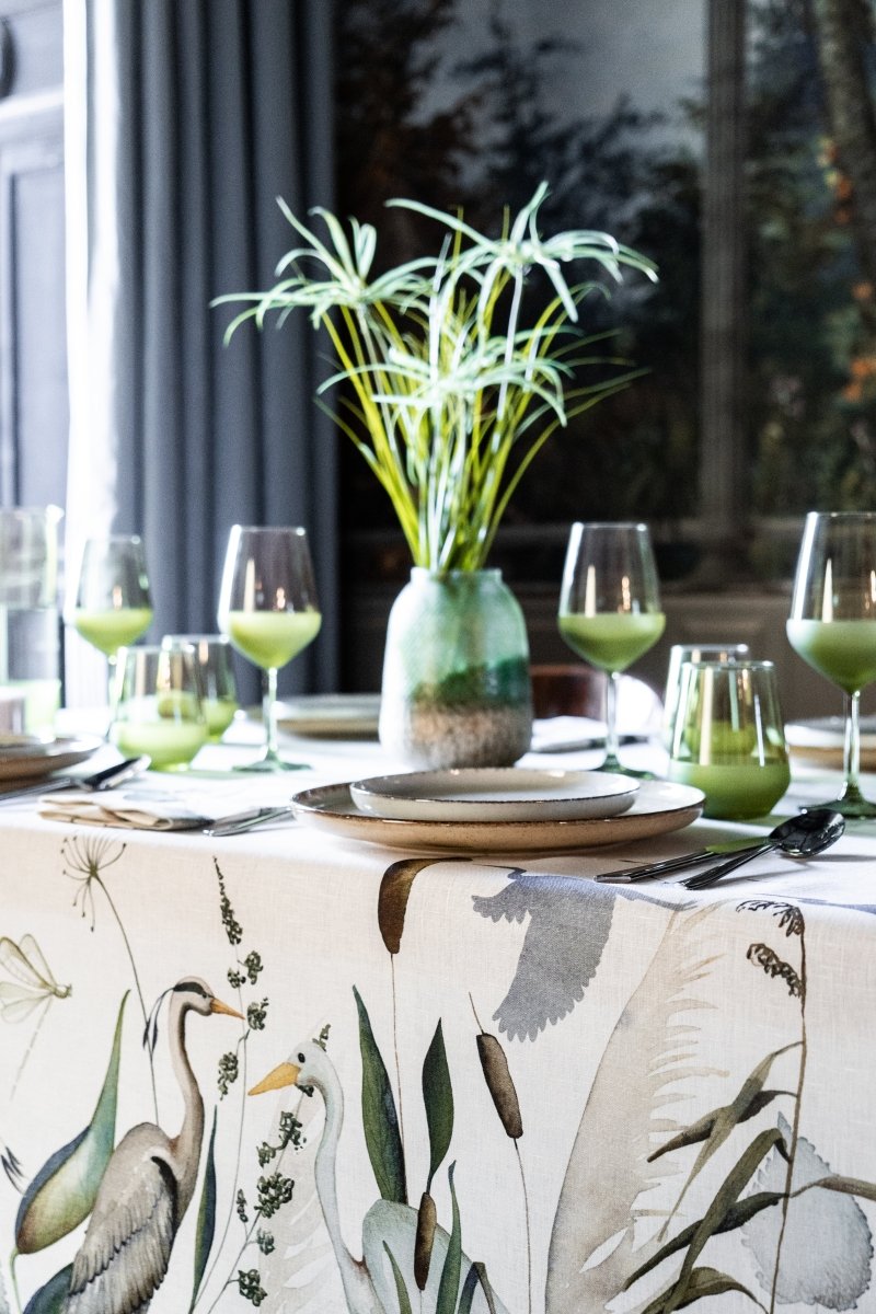 Dining table setting with a botanical tablecloth, greenery, and wine glasses.