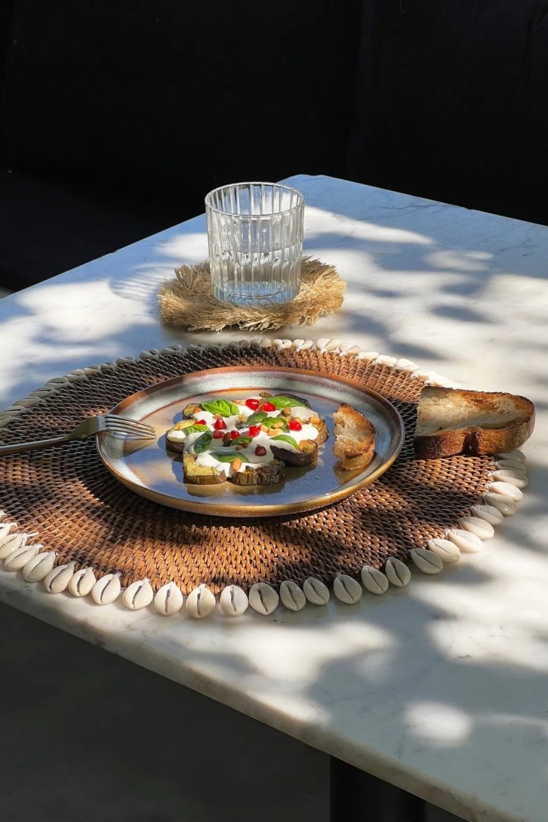 Plated dish with salad and bread on a textured placemat, glass on a coaster, on a marble table.