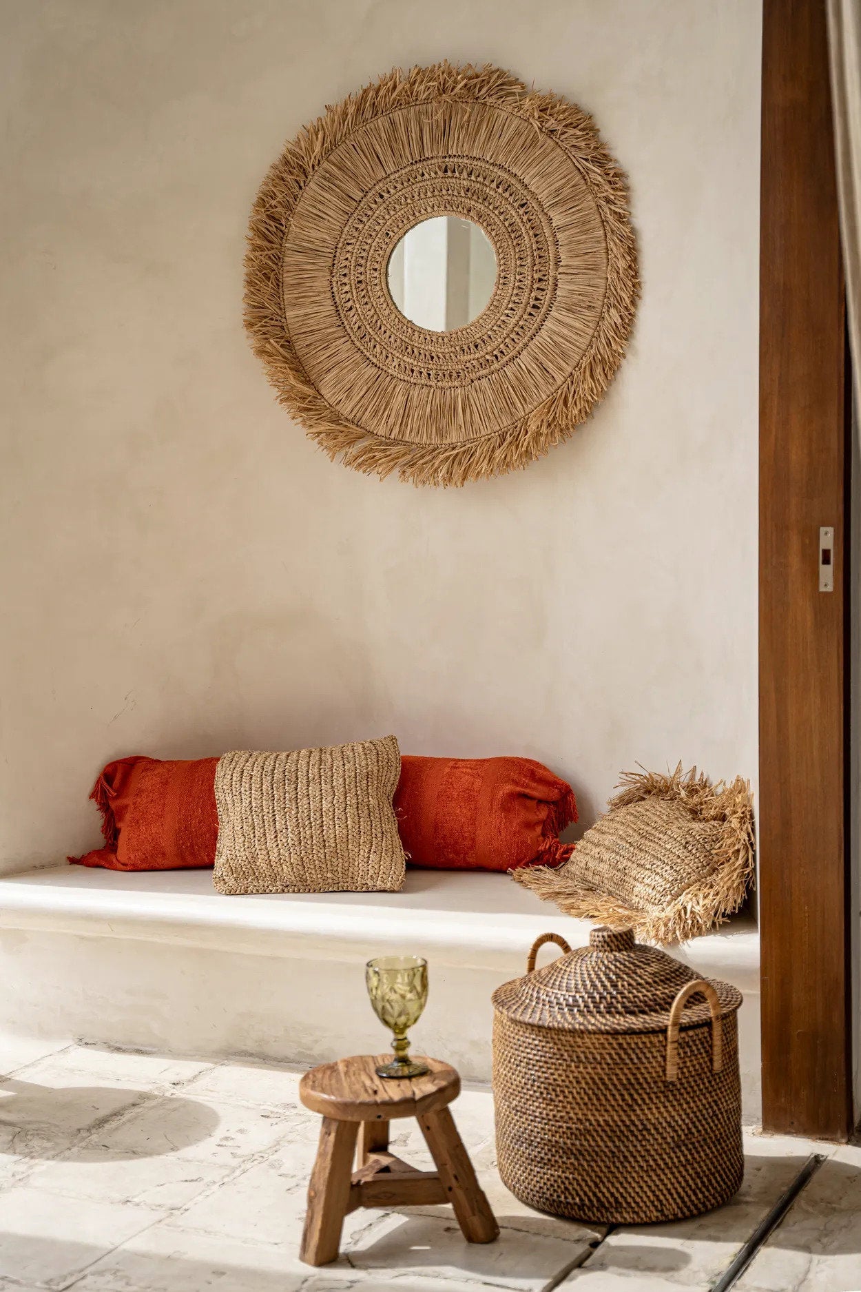 Woven mirror on a wall above a seating area with pillows and a small table.