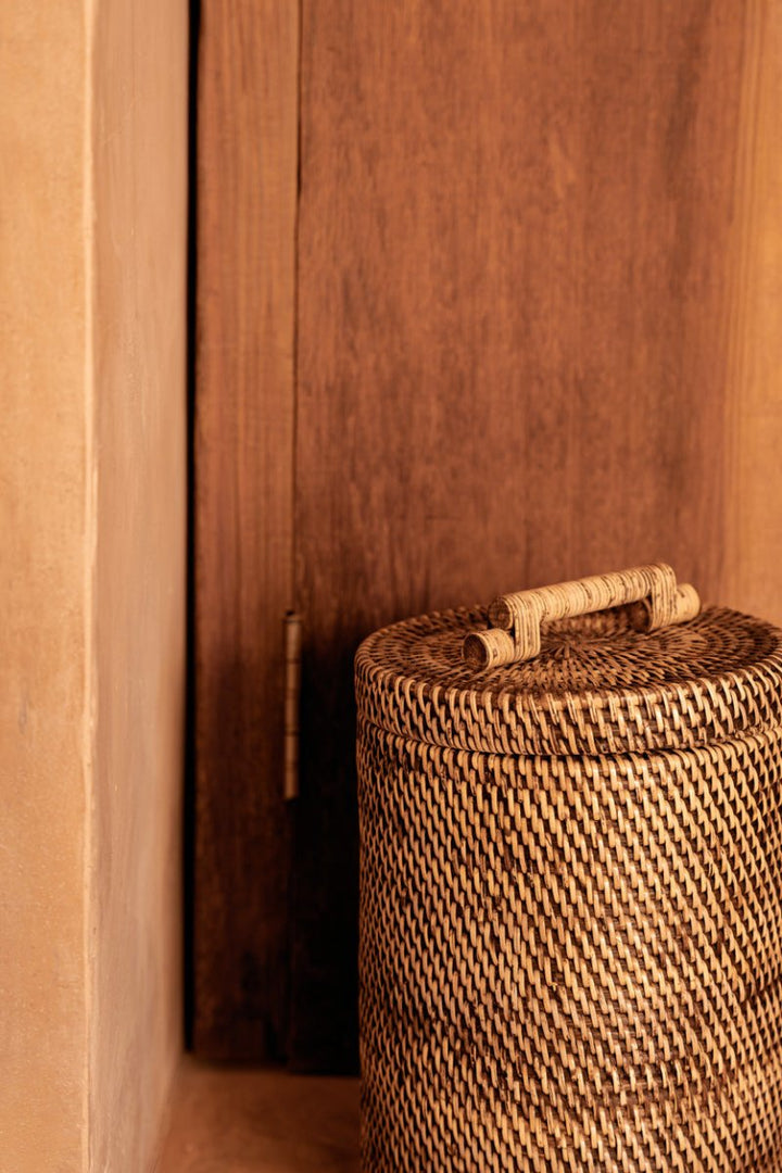 Woven basket with a lid against a wooden wall.
