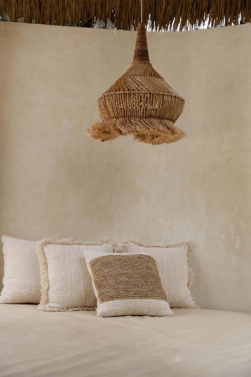 Woven pendant light hanging above textured pillows against a beige wall.