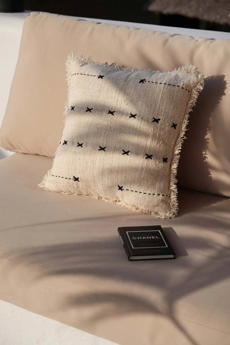 Beige pillow with black patterns on a beige surface, with a Chanel wallet in the foreground.