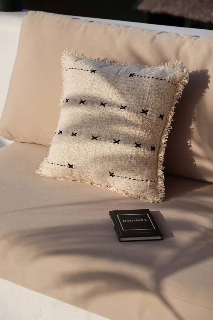 Beige pillow with black patterns on a beige surface, with a Chanel wallet in the foreground.