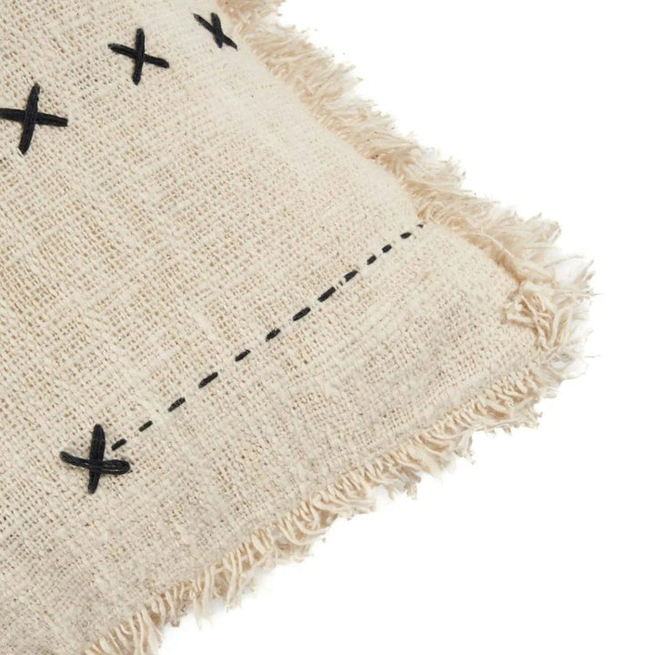 Beige woven cushion with black cross patterns and frayed edges on a white background