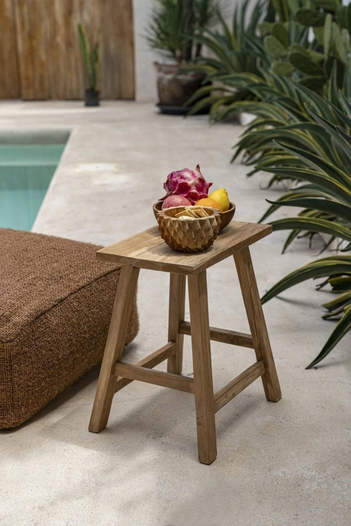 Wooden stool with a bowl of fruit by a poolside