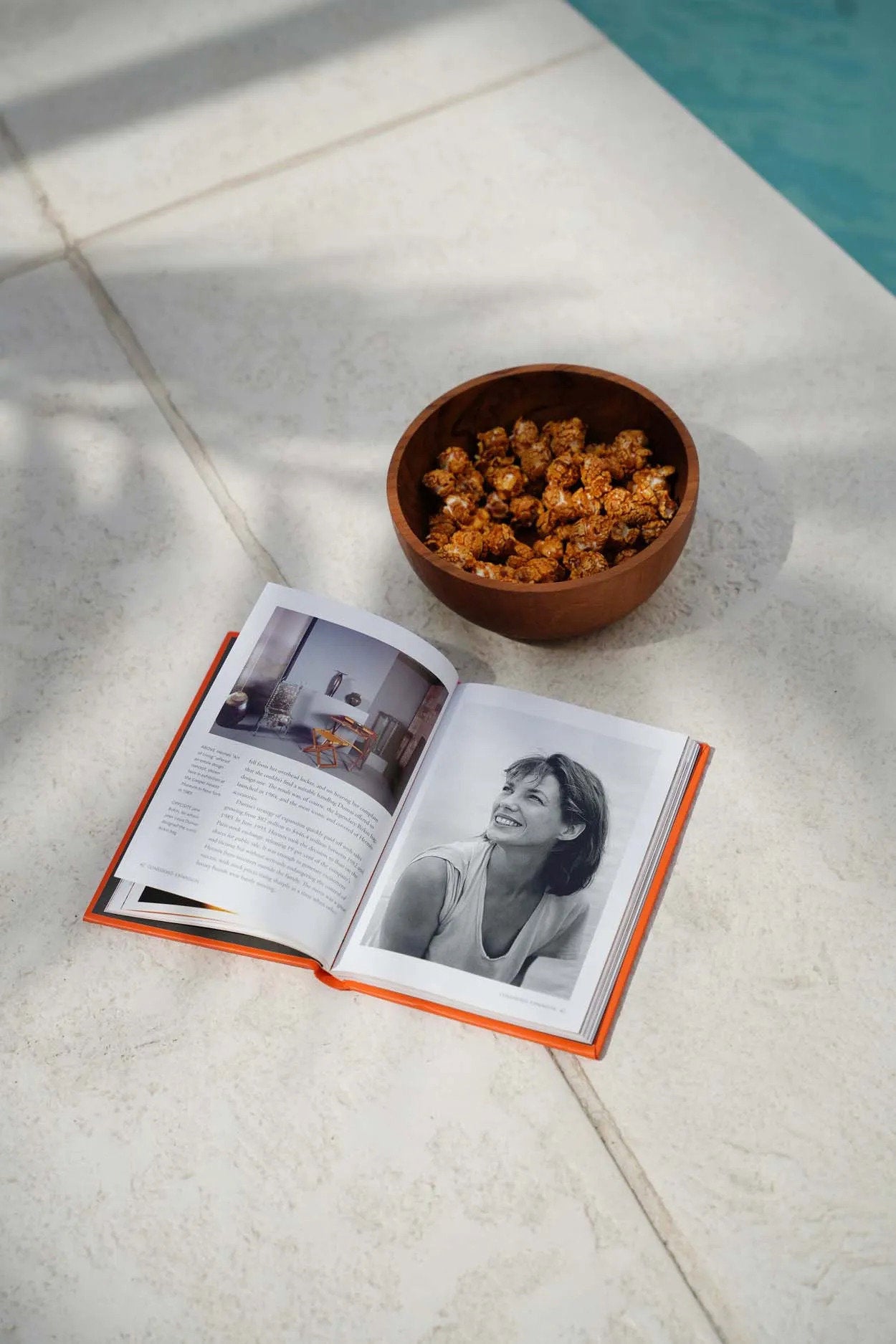 Open book with a bowl of snacks on a tiled floor near a pool