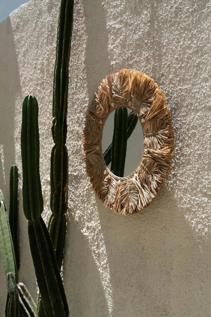 Round woven mirror on a textured wall with cacti in the foreground