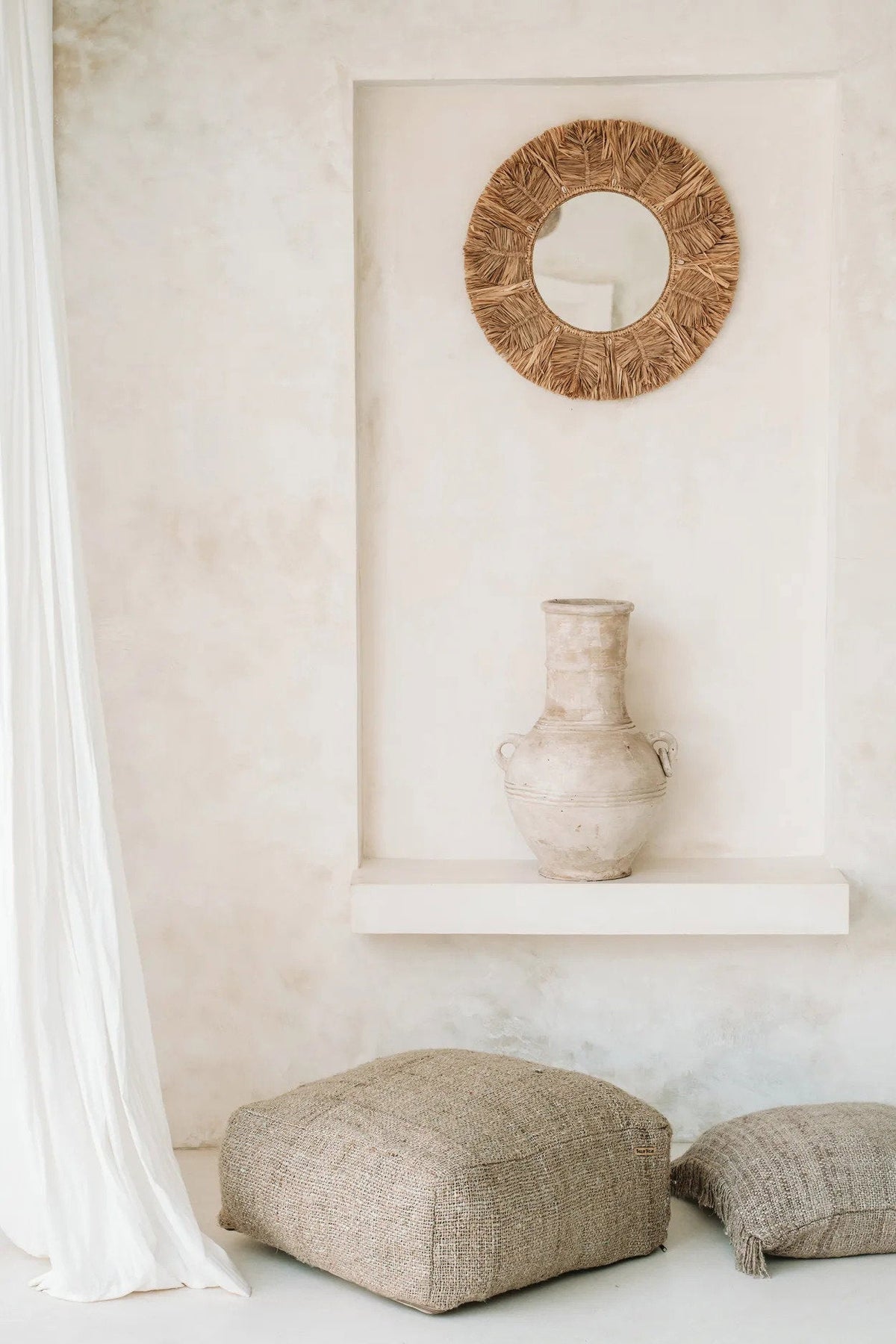 Decorative mirror and vase on a shelf against a white wall with textured floor cushions.