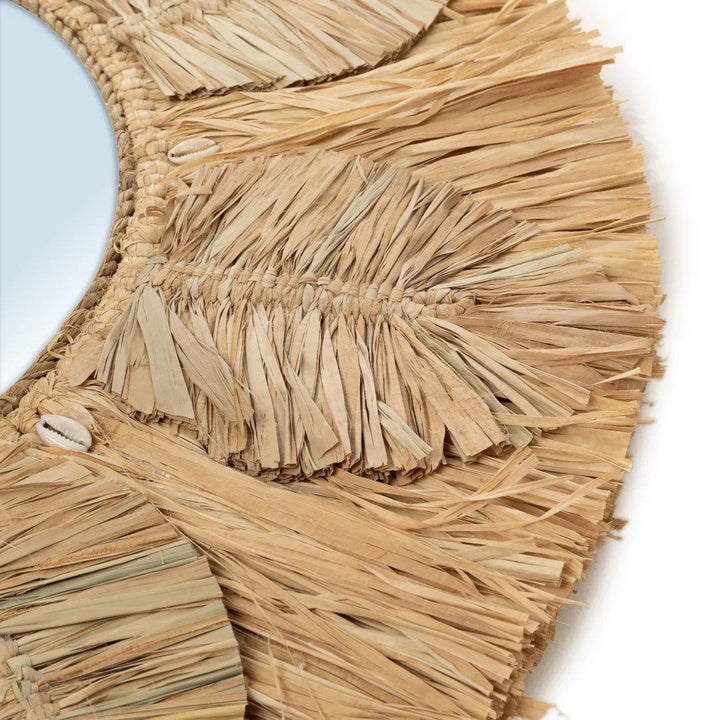 Close-up of a woven straw wall art piece with fringes on a light blue background