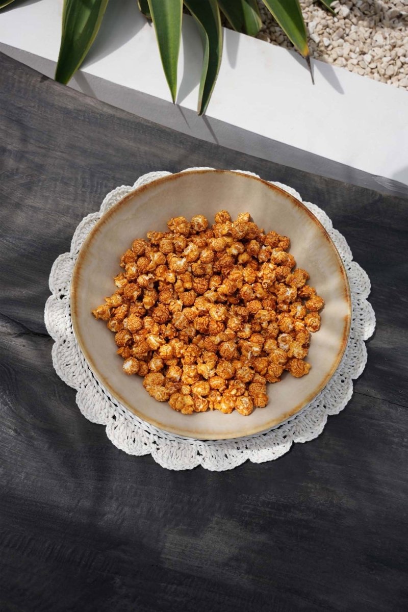 Bowl of popcorn on a textured surface with a plant in the background